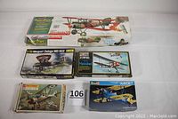 Five boxed aircraft model kits arranged on white surface including a large balsa wood kit and four plastic 1/72 scale aircraft kits