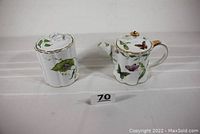 Front view of porcelain teapot and canister decorated with butterflies and flora showing the overall shape, designs, and gold accents.