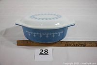 Side view of blue Pyrex casserole dish with lid in place on ruler for size reference.