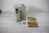 Original box for the Pillsbury Poppin' Fresh ceramic bank placed next to a slow cooker recipe booklet on a white surface. Box shows slight dirt, intact condition.