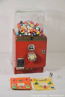 Front view of the vintage red Northwestern gumball machine filled with colorful gumballs and two prize cards displayed in front.