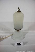 Front view of the complete lamp with opaque cylindrical glass shade and square glass base on a white surface