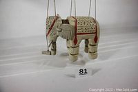 Photo of vintage white hand-carved wooden African elephant marionette with red trim and holes detail, hanging by marionette strings showing front and side view.