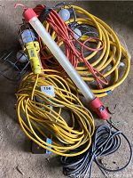 Photo showing several coiled extension cords in yellow and black, multiple trouble lights with metal cages, and one fluorescent-style trouble light with red ends.