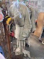 3 photos showing ArcGuard safety suit set hanging on a rod including overalls, topcoat, and face shield with visible stains and industrial background.