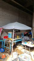 White canopy tent set up in warehouse environment with various items in background, showing overall structure, top and close-up of fabric condition.