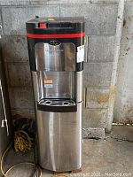 Front view showing the water dispensing area labeled Viva Self Clean, stainless steel body, black top with red stripe and attaching power cord.