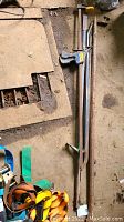 Two long steel crowbars and one long bar clamp with Quick-Clip grip and rust, laid on the floor.
