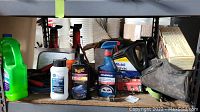 Photo showing two 1/2 ton red hydraulic jack stands, Mobil Delvac 1300 Super oil container, Simoniz spray tire cleaner and paint restorer, Meguiar's Ultimate Polish and other automotive fluids and accessories on shelving.