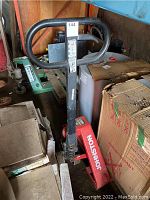 Full view of red Johnston pallet jack showing handle, forks and surrounding inventory