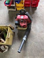 Top view of Redmax backpack leaf blower showing red engine housing, black air intake and yellow fuel tank, with hose extending forward.