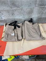 Two folded beige overalls laid flat on a table, showing their fabric and overall condition including some stains.