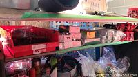 Shelf with organized items including boxes of parts, electrical components, and rolls of red caution tape with black text
