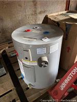 Overview of the gray cylindrical water tank showing top and partial side with connection points and warning labels.