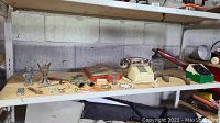Photo showing an assortment of vintage items on a wooden shelf including a cream rotary phone, metal figurines, and small collectibles.