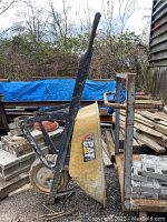 Side view of the yellow CAT wheelbarrow showing black metal handles, wheel, and rusted frame with faded CAT logo on the tub.