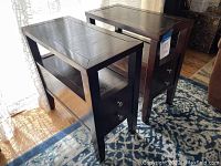 View of two dark brown wood end tables showing rectangular tops, open shelves, and drawers with metal knobs