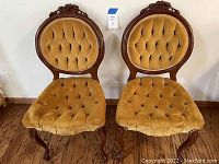 Front view of two yellow velvet Victorian side chairs with carved wood frames and button-tufted upholstery.