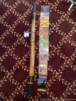 Full view of the didjeridu placed on patterned carpet alongside a set of instructional didjeridu booklets in various colors.