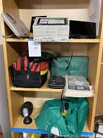 Photo of shelving with the entire lot including two Garmin navigation systems, travel kits, sewing kit, bag, and light.