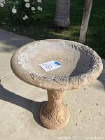 Full view of the birdbath showing the decorative basin rim and embossed pedestal with butterflies and flowers in natural sandstone color.