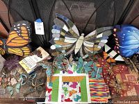 Overview of butterfly collection showing various stained glass butterfly decorations in blue, orange, and multicolor, fabric quilt piece with butterfly print, and several butterfly ornaments on a table.