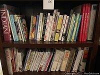 Bookshelf with two shelves containing a variety of cookbooks, most spines showing titles related to vegetarian, vegan, dessert, bread, and Mediterranean cooking. Various colors and sizes, mostly hardbound and paperback.