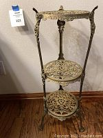 Full front view showing the three-tier brass stand with intricate filigree pattern on round shelves, three supporting legs with decorative details, and claw feet.