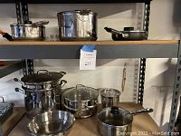 Wide shot showing shelves with various stainless steel pots, pans, lids, and fryer basket arranged neatly.