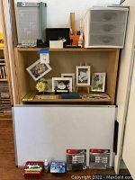 Wide photo showing wooden shelving unit with various art supplies, photo holders, dry erase board and storage drawers