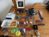 Wide view of vintage collectible buttons, assorted medals, and knives on wood surface.