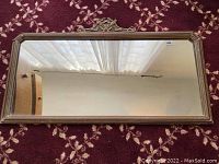 Front view of the rectangular vintage mirror capturing the reflective glass and ornate frame detail atop.