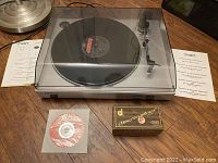 Photo showing ION USB turntable with clear plastic dust cover, software installation disc, instruction manual, USB video input connector, and a Discwasher cleaning kit box.