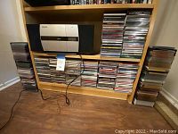 Full view of the Jensen CD player sitting in shelf surrounded by large stacks of CDs and two metal CD towers