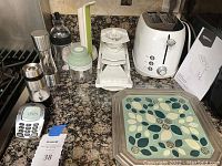 Wide view showing all items including toaster, mini chopper, grinders, timer, paper towel holder, mandolin slicer and trivets on kitchen counter.