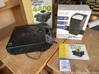 Overall view of the Kodak Carousel 4400 slide projector on wooden surface with its original box behind it, alongside the VuPoint digital film scanner box and projector manual.