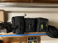 Wide shot of the three upright rolling luggage pieces and two duffel bags on shelf.