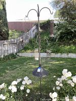 Full view of the metal garden pole with all hooks and bird feeders hanging, situated outdoors in garden area with flowers and greenery.