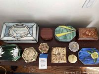 Photo of 12 various decorative boxes displayed on a wooden surface including stained glass, wooden, stone, and glass boxes in various shapes and sizes