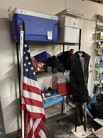 Blue and red plastic coolers on metal shelving, with white foam cooler and black vests hanging.