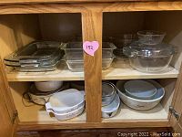 Shelf containing stacked clear Pyrex glass loaf pans and rectangular baking dishes on top shelf, tan and brown Pyrex mushroom design bowls, and blue, white Corningware bowls on bottom shelf