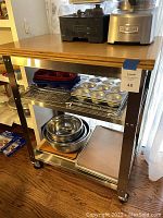 Front view of rolling kitchen cart showing wood block top and stocked metal wire shelves holding kitchen baking items like muffin pans, mixing bowls.