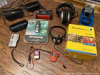 Photo of entire lot including Rosetta Stone Spanish language CD set, voice recorders, headphones, MP3 players, Fitbit devices, emergency radio, and alarm clocks arranged on wooden surface.