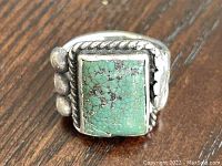 Close-up photo of the vintage men's silver ring with a rectangular turquoise stone set in an ornate silver frame with rope and bead detailing.