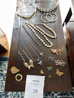 Top-down photo of assorted jewelry including crystal tiara, chokers, pearl necklaces, chain necklaces, butterfly pins, hoop earrings, bracelets.