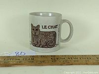 Side view of Tamil & Ng Le Chat mug showing the cat graphic and French text on ceramic mug with a ruler for size reference.