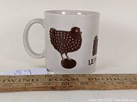 Side view of the white ceramic mug showing brown chicken illustration and part of 'LE POULET' text.