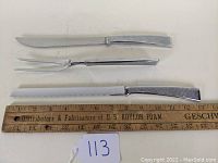 Display of carving knife, carving fork, and serrated bread knife laid next to a ruler for size reference.