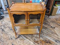 Front angle view of the antique wooden stand showing mesh-paneled double doors and lower shelf.