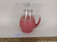 Clear side view of glass pitcher showing salmon pink frosted lower half, clear upper half, handle, and gold band.
